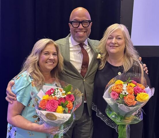 two female ward winners holding flowers standing with presenter